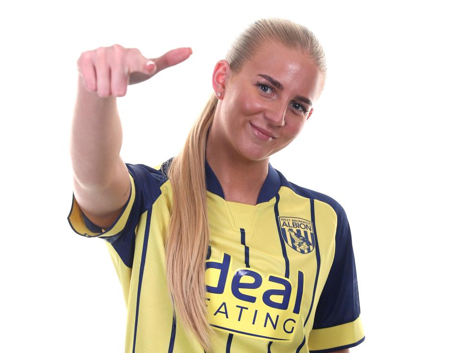 Rhianne Oakley smiling and pointing at the camera while wearing the yellow and blue away shirt 