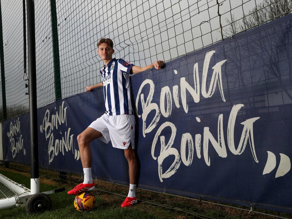 Isaac Price in the home kit posing for a photo next to a sign which says 'Boing Boing'