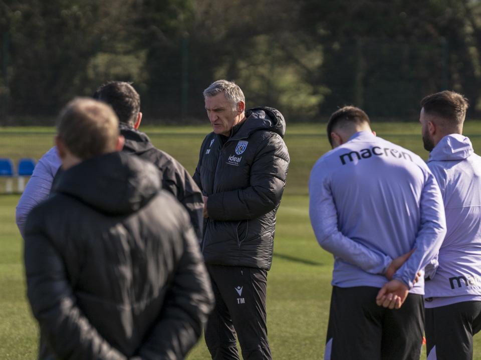 Tony Mowbray on the training pitch in a black WBA coat talking to players and staff
