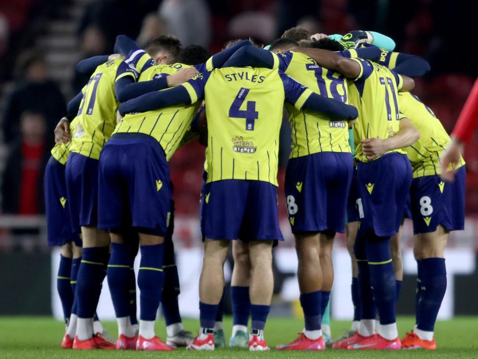 Albion players in a huddle before a game wearing the yellow and blue away kit 