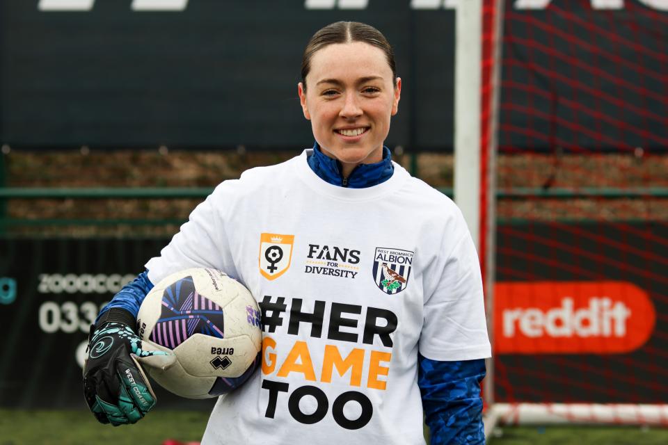 Anna Miller smiling at the camera holding a ball while wearing a Her Game Too t-shirt
