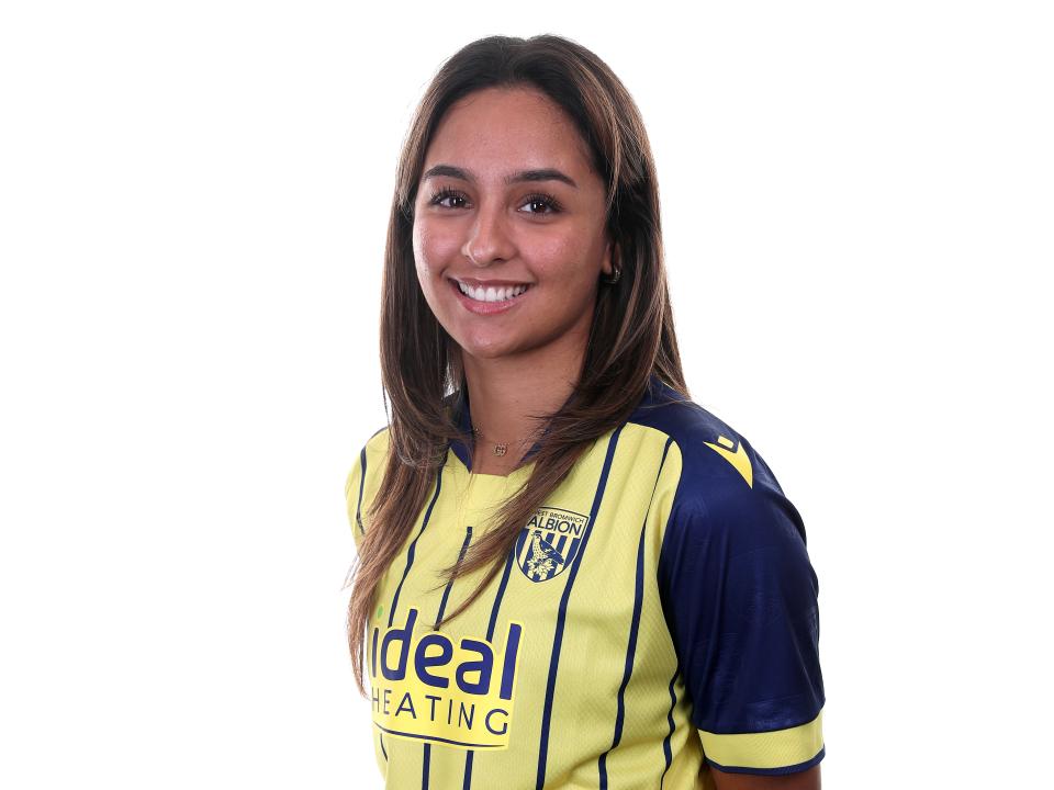 Maz Mahmood smiling at the camera while wearing a yellow and blue away shirt