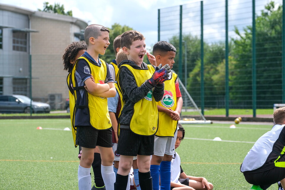Participants wearing Kelloggs Football Camp bibs, smiling and clapping