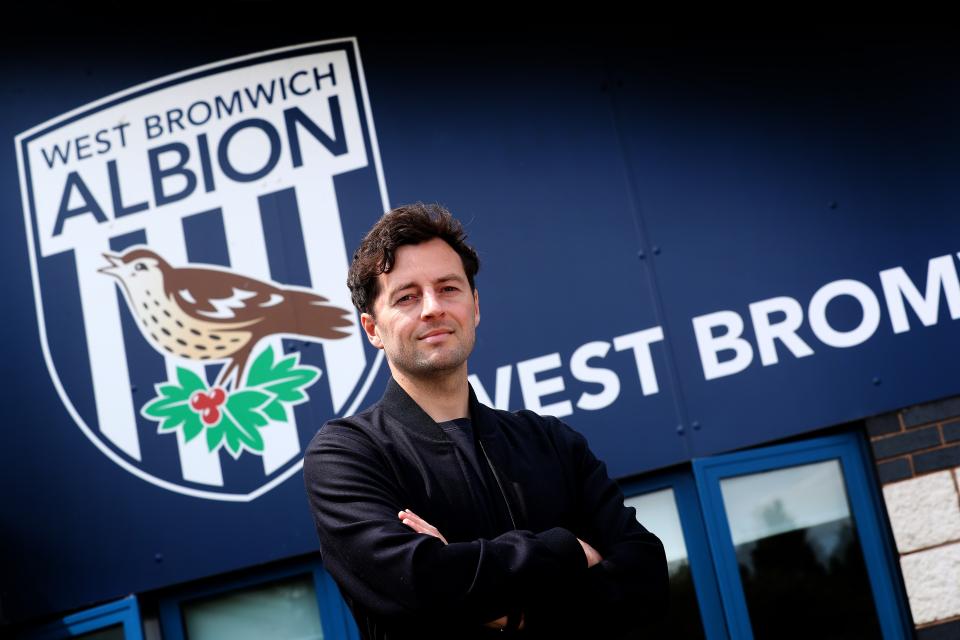 Ryan Mason posing for a photo with his arms crossed and a smile on his face looking at the camera while stood in front of WBA branding 