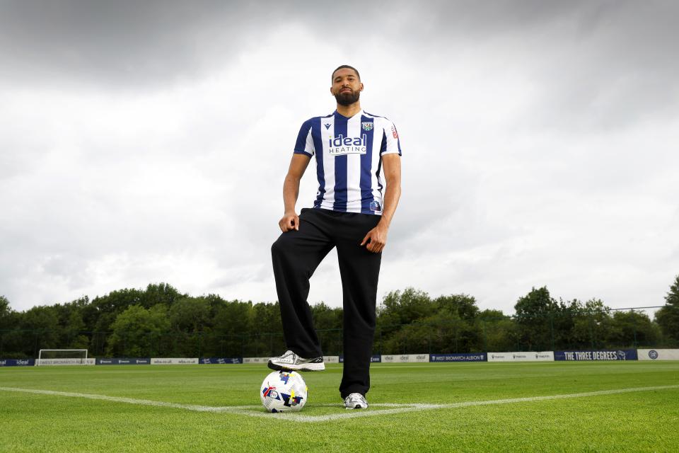 George Campbell stood in the middle of a training pitch in a home WBA shirt with his foot on a ball while smiling at the camera 