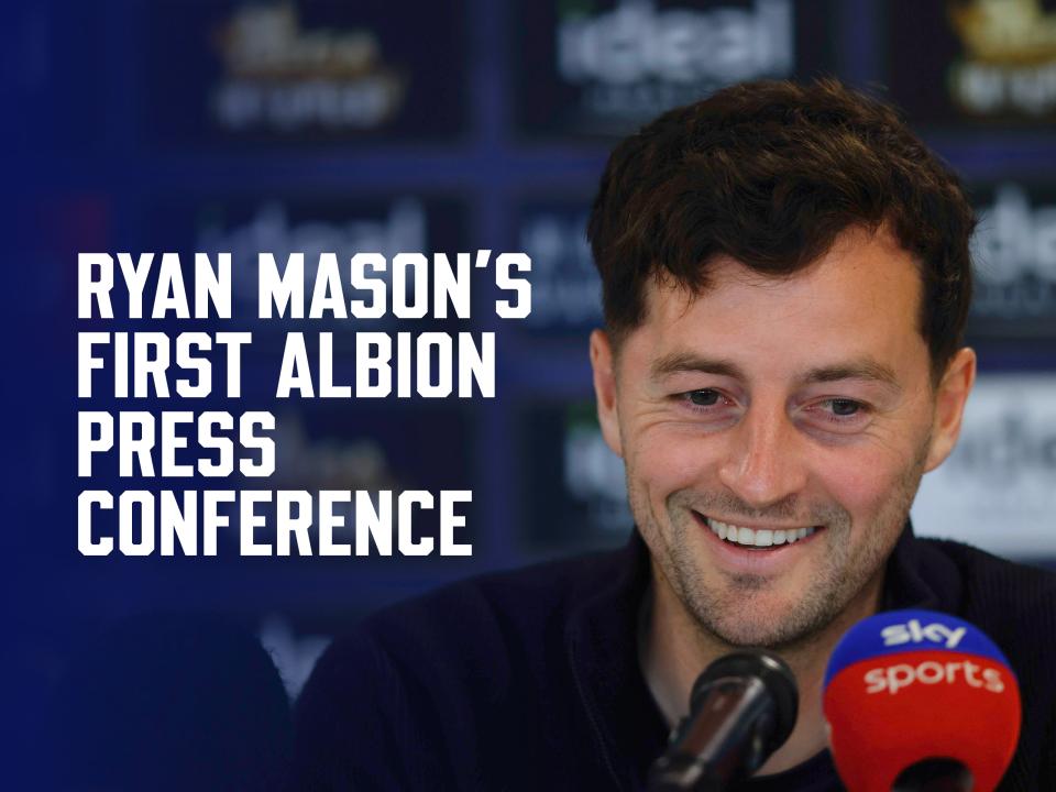 Ryan Mason speaking to the media in front of sponsor boards with a smile on his face