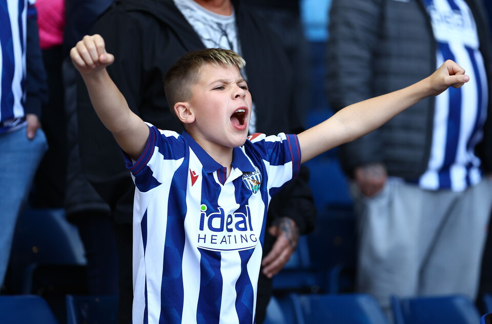 A young WBA fan cheering in the stand with a home WBA top on