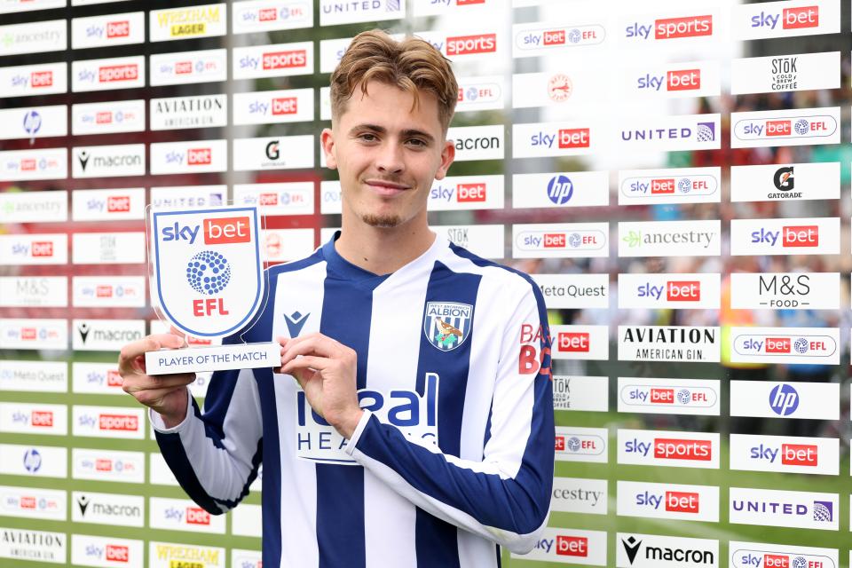 Isaac Price smiling at the camera while holding up a Man of the Match trophy in the home kit 