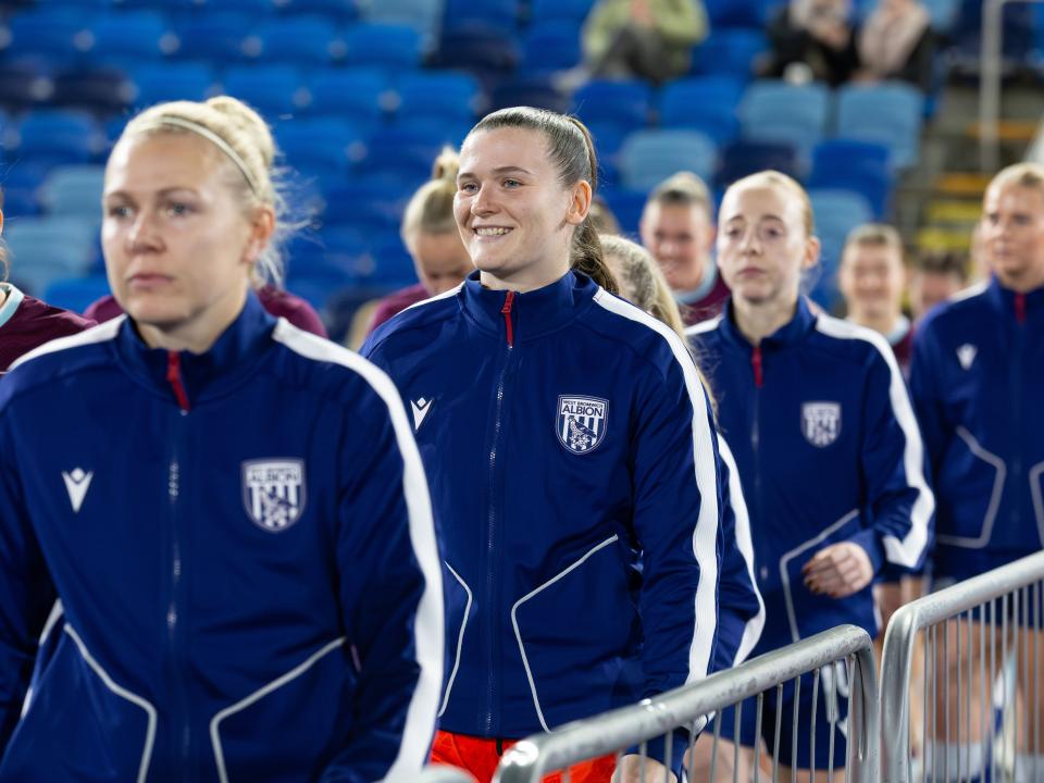 Charlotte Clarke smiling as she walks out ahead of a game with an Albion tracksuit on 