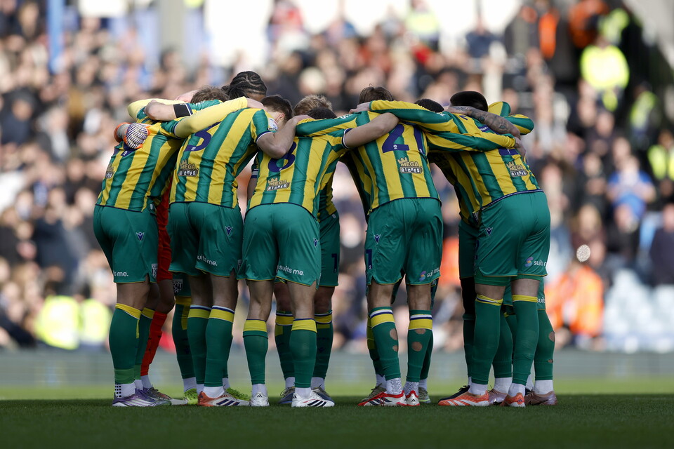 Albion players in a pre-match huddle before an away game in the green and yellow away kit 