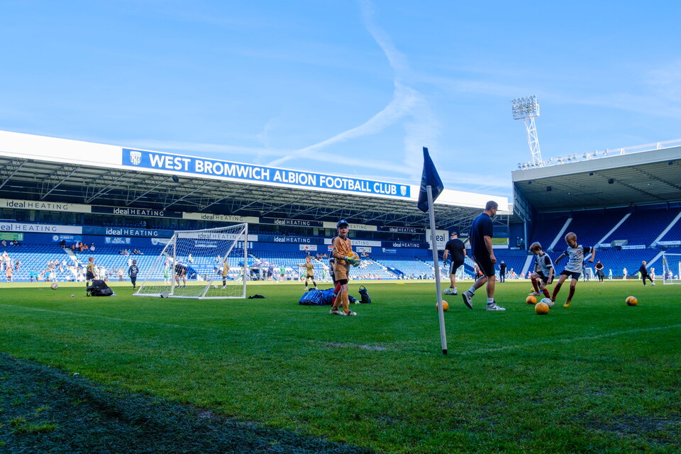 Players warming up on the pitch with the West Stand in the background.