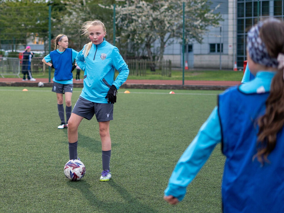 Player with ball at her feet, players in bibs in the background.