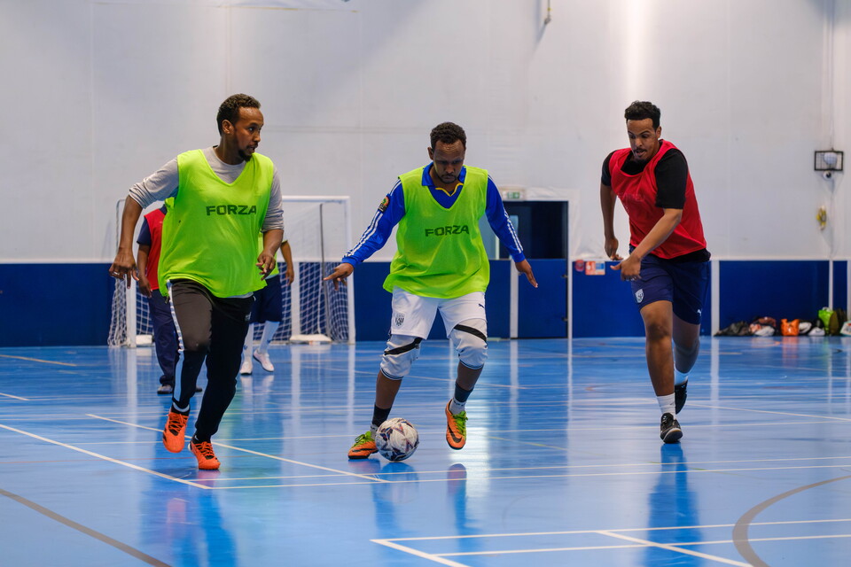 Player with the ball at his feet with teammate in support and defender chasing in the WBA Community Sports Hall