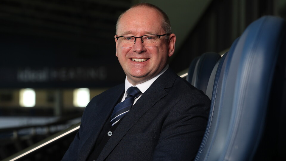 Mark Miles smiling at the camera while sat in a seat at The Hawthorns