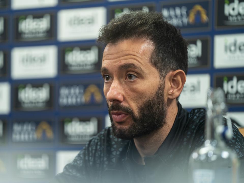 Carlos Corberan is pictured in a press conference in front of advertising boards