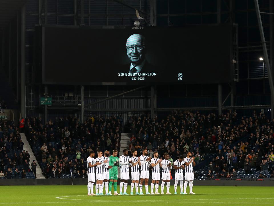 Albion players on the centre circle in a line with an image displayed of Sir Bobby Charlton behind them on the big screen