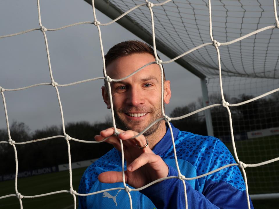 Andi Weimann smiling at the camera through a goal net
