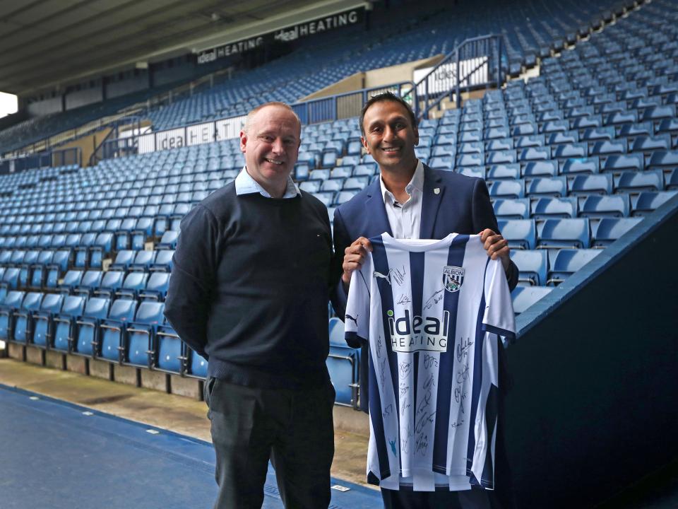 Shilen Patel poses for a photo with West Bromwich Albion's Managing Director Mark Miles while smiling and holding up a home Albion shirt