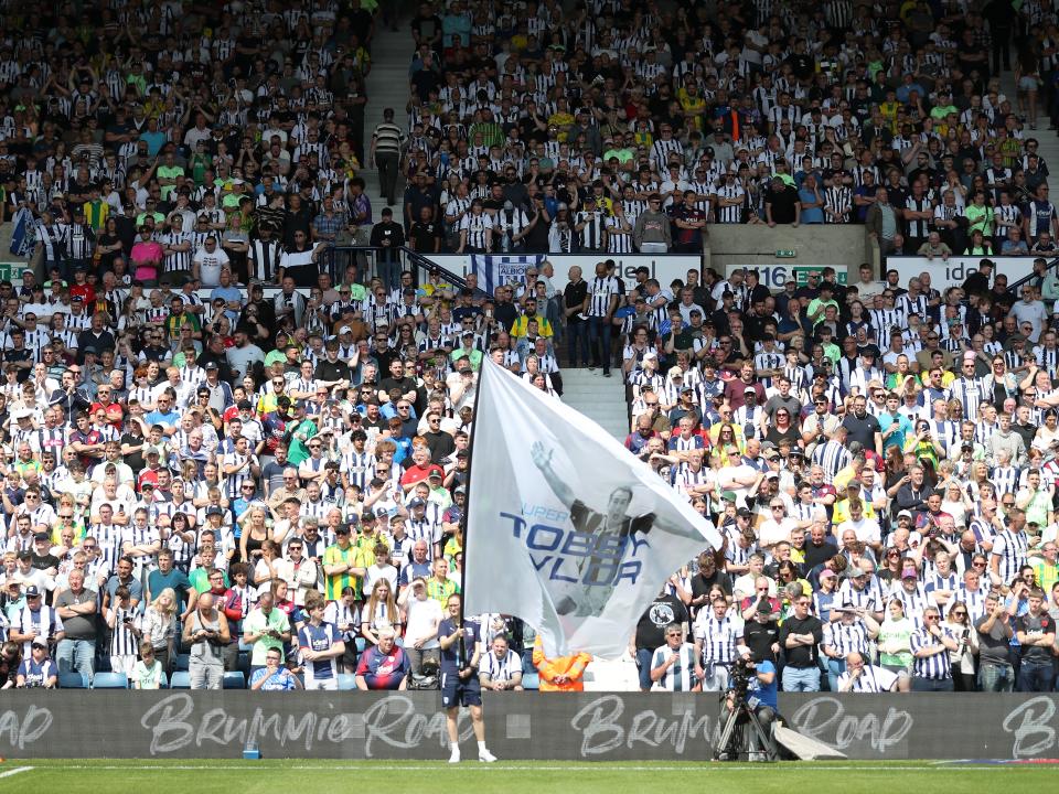 A huge flag is waved on the side of the pitch with hundreds of Albion fans behind it