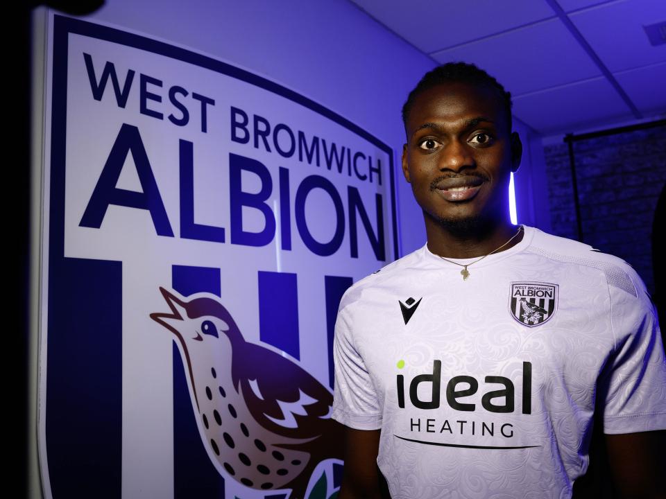 Ousmane Diakité smiling at the camera while stood next to a big WBA badge 