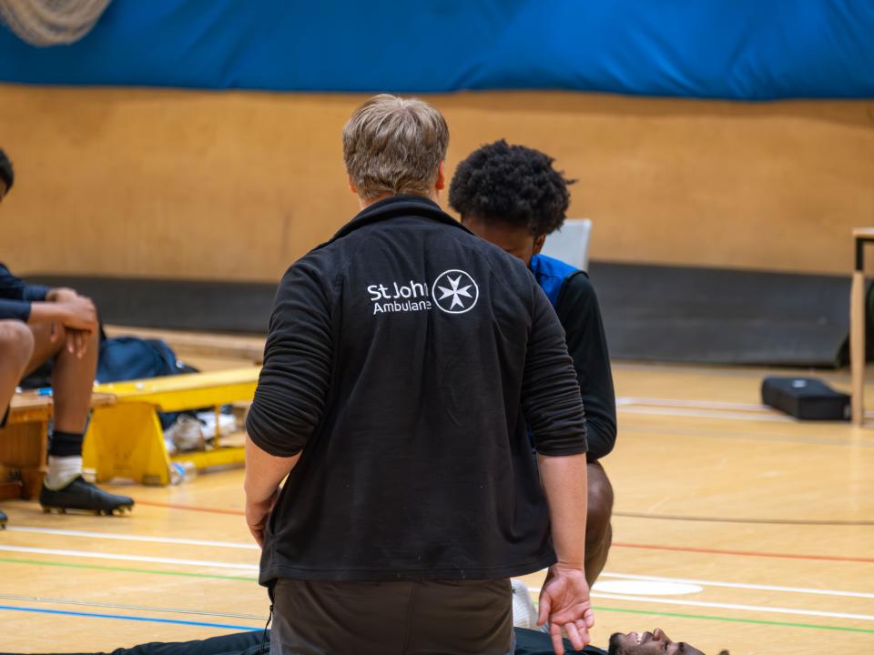 St John's Ambulance tutor (back to camera) demonstrating how to check for danger.
