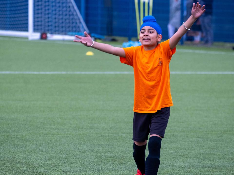 A player wearing orange holds his arms outstretched during the South Asian Emerging Talent Festival on the Academy pitch.