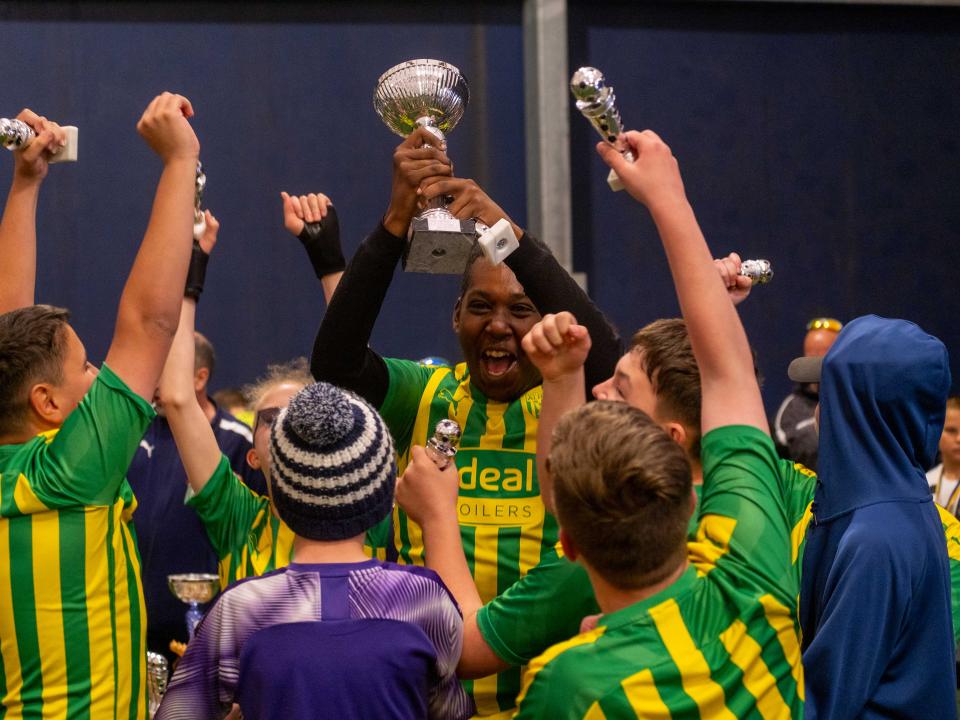 A group of Albion players lift one of the Sandwell Inclusion Cup trophies wearing the Baggies' 2019/20 green and yellow away shirt.