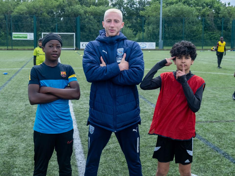 Jordan Hall, youth engagement coach, stands either side of two children doing a goal celebration.
