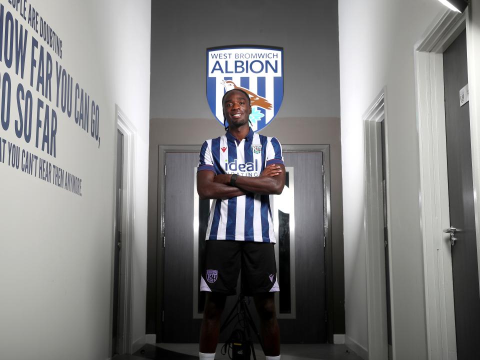 Devante Cole with his arms crossed smiling at the camera wearing a home shirt 