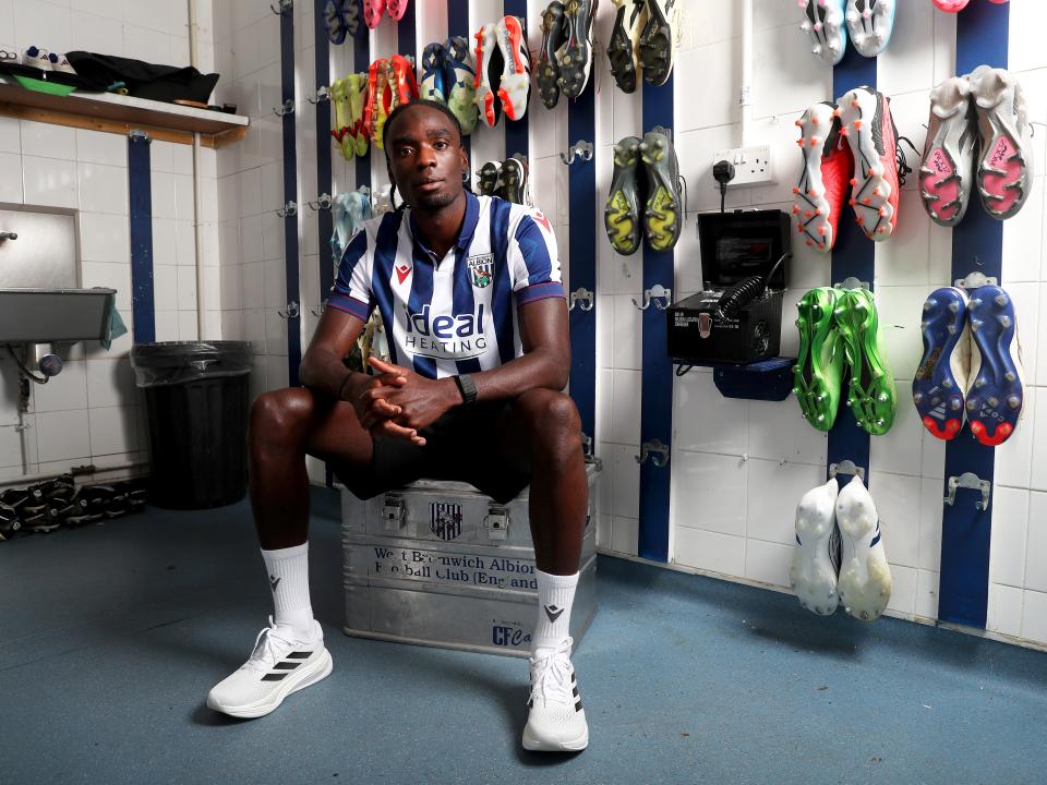 Devante Cole staring at the camera in a home shirt while sat in the boot room