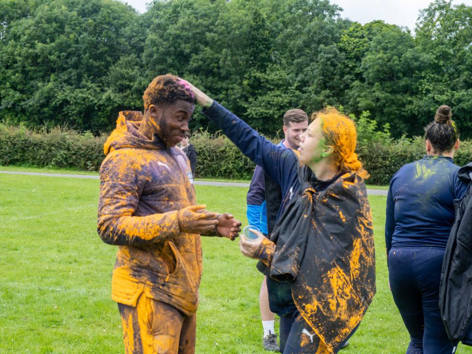 Two Foundation staff members covering each other with orange paint powder