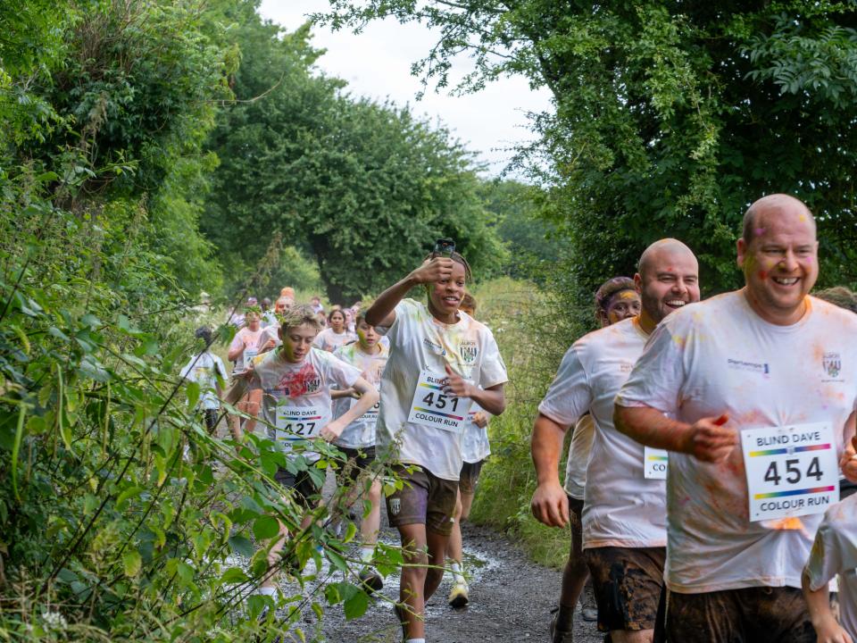 Runners heading through shrubs on Sandwell Valley Park. One participant recording on his phone.