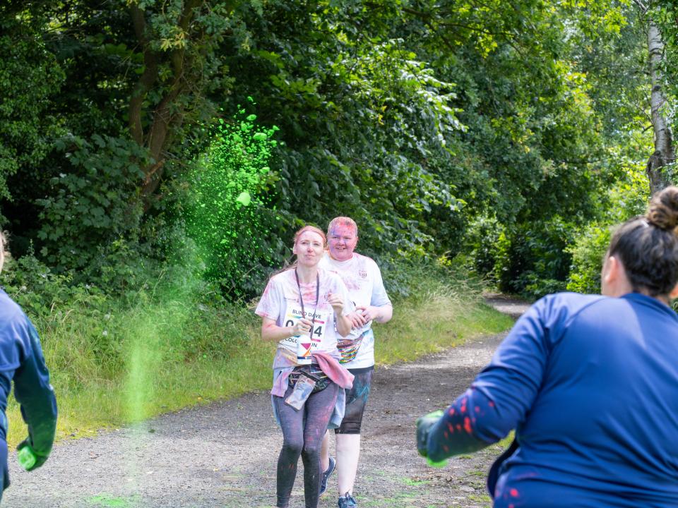 Two participants running towards Foundation staff at a colour station, throwing paint powder.