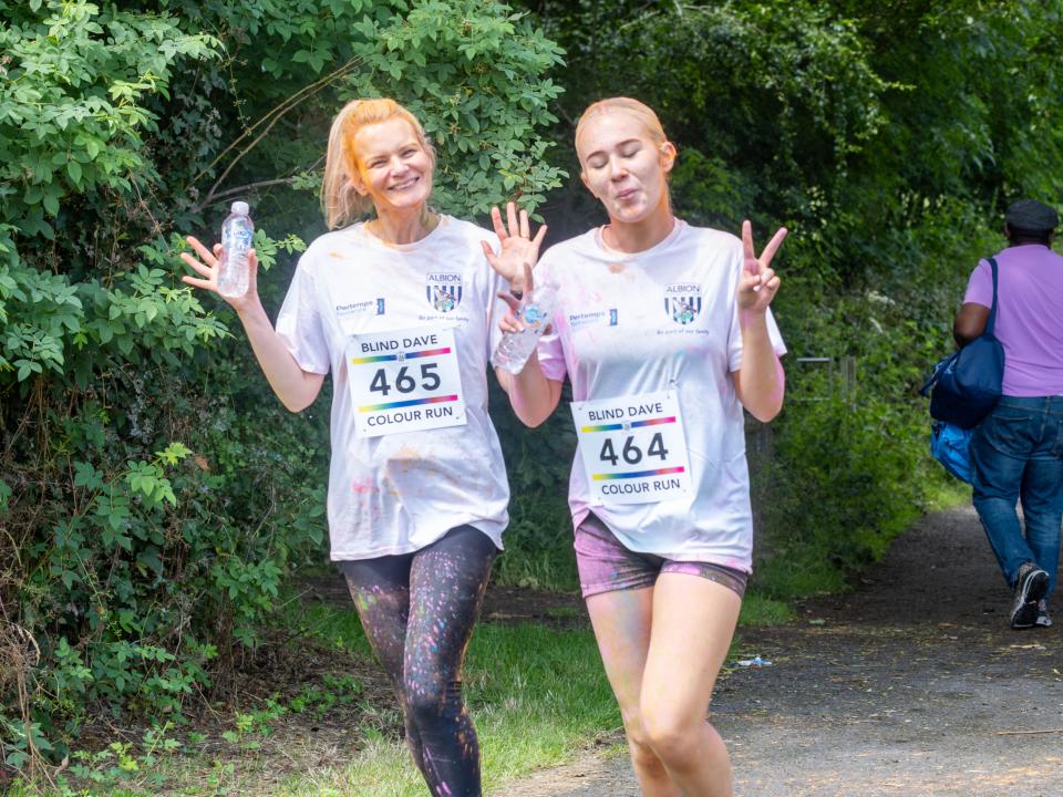 Two female participants holding water bottles and smiling showing peace sign .