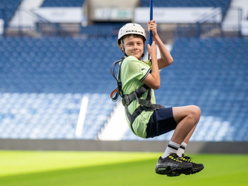 A child soars across The Hawthorns holding onto the Zipwire with two hands.