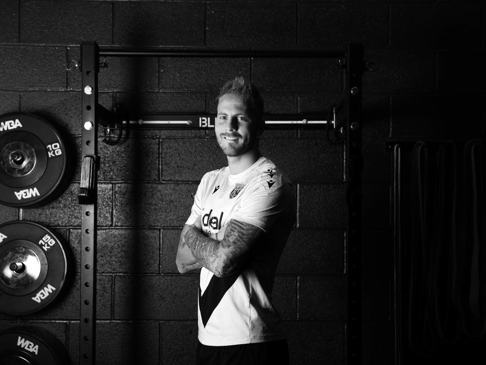 A black and white image of Uroš Račić smiling at the camera while stood in the gym