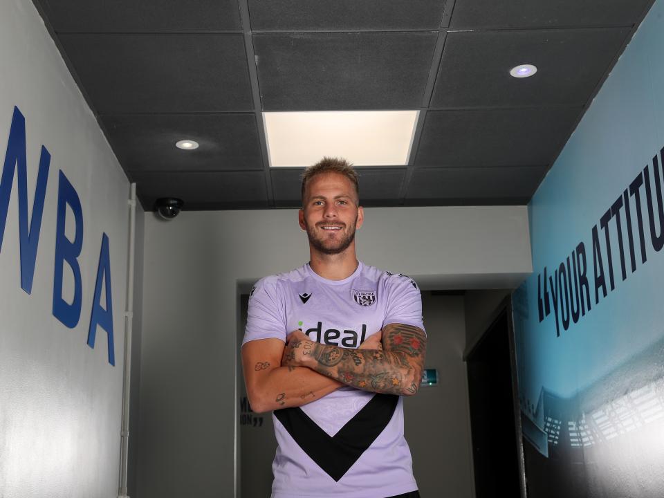 Uroš Račić smiling at the camera while stood in a corridor with his arms folded 