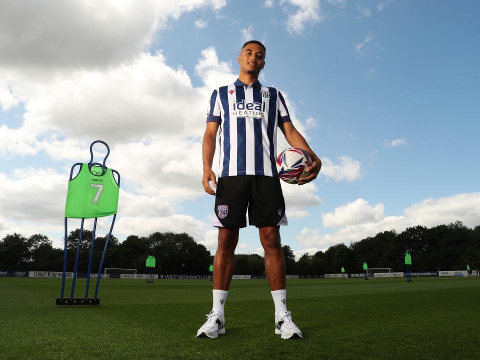 Lewis Dobbin smiling at the camera while stood on the training pitch in a home shirt holding a ball