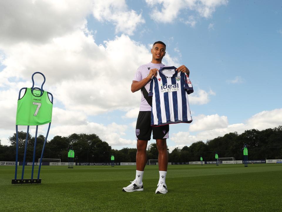 Lewis Dobbin smiling at the camera while holding a home shirt up while stood on a training pitch 