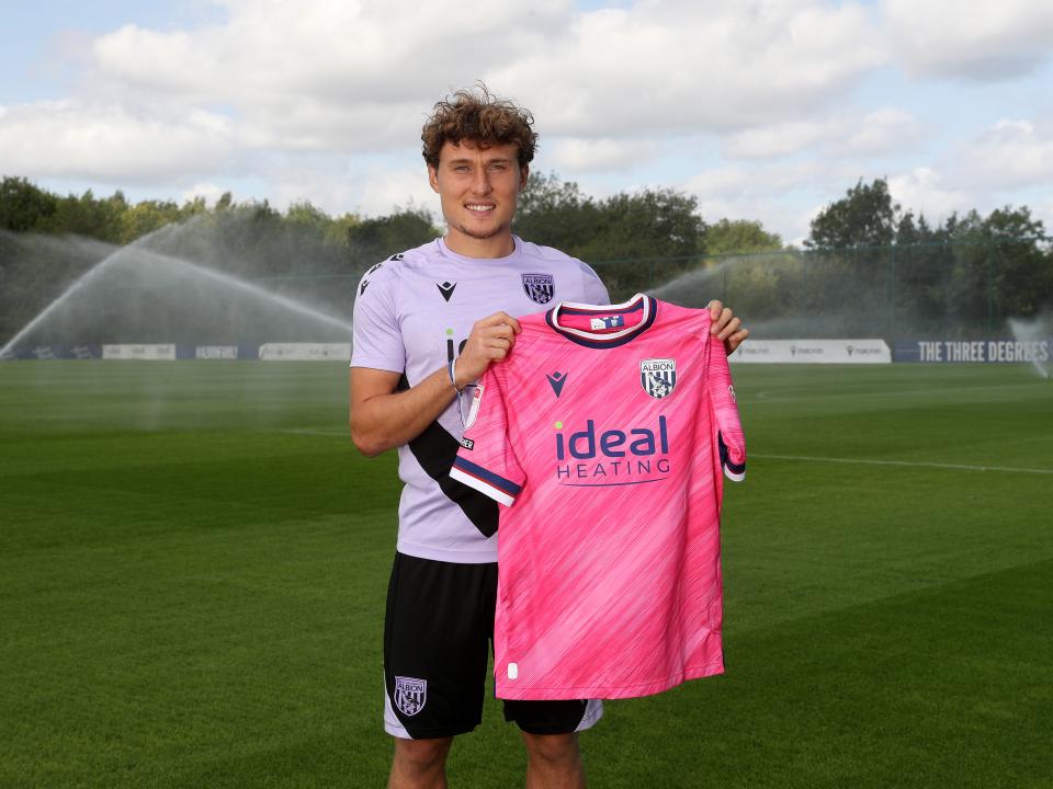 Callum Styles smiling at the camera while holding a pink away shirt 