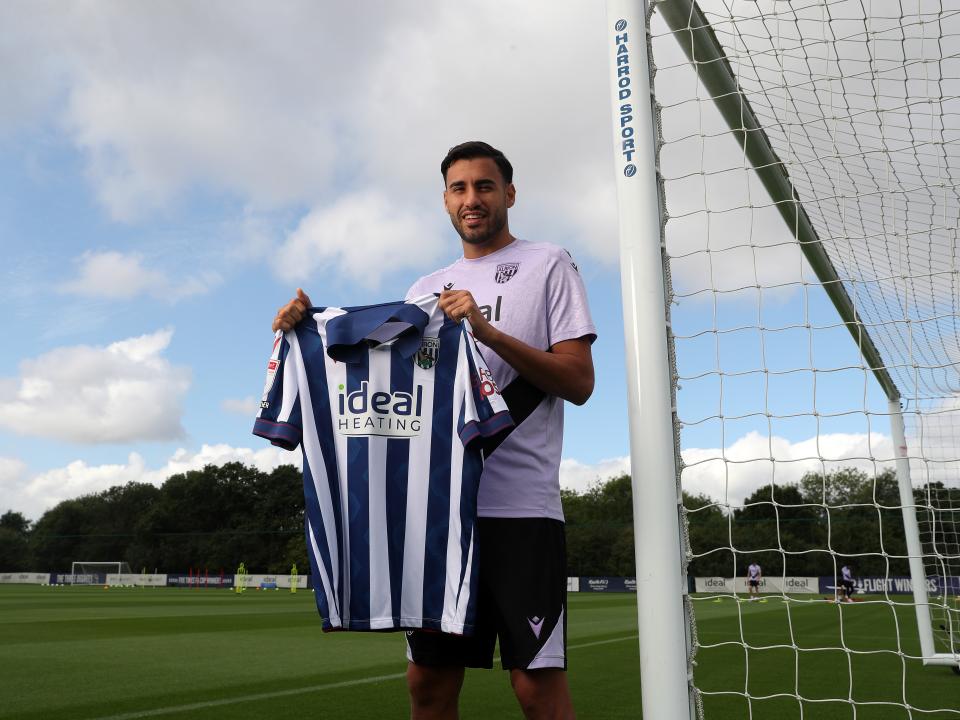 Gianluca Frabotta smiling at the camera while stood against a goal post holding up a home shirt 