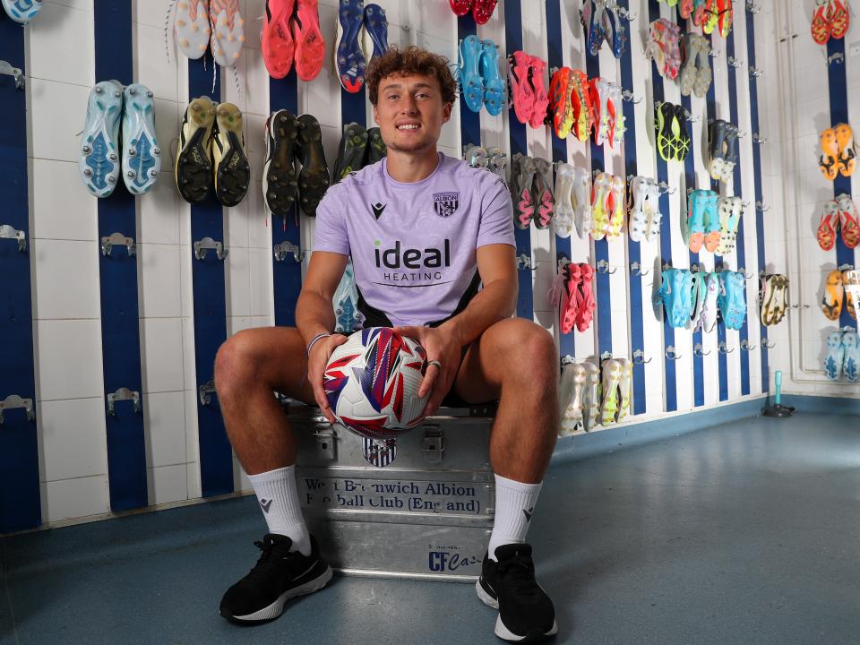 Callum Styles smiling at the camera while holding a ball sat in the boot room 