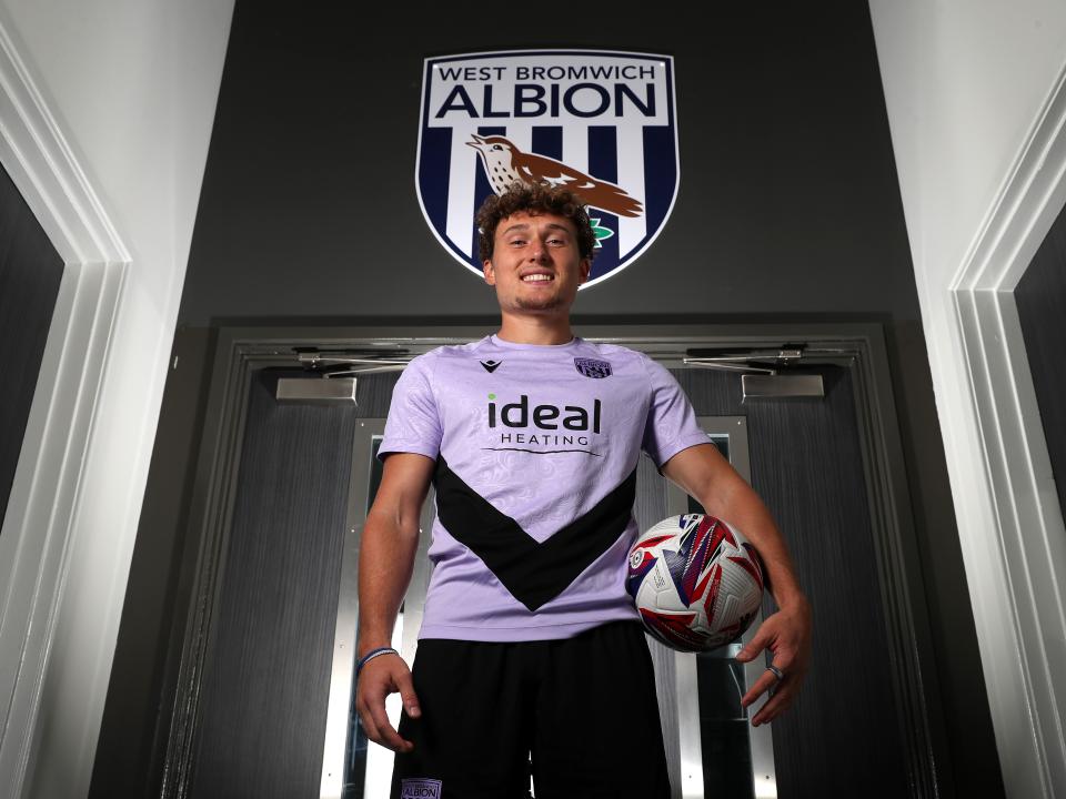 Callum Styles smiling at the camera while holding a ball while stood in a corridor 
