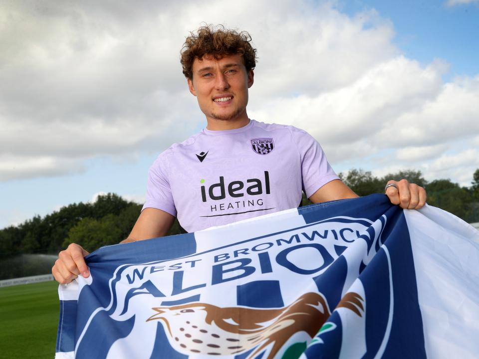 Callum Styles smiling at the camera while holding a WBA flag