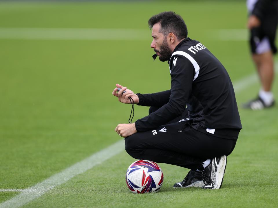 Carlos Corberán watching training crouched down with a whistle and a ball