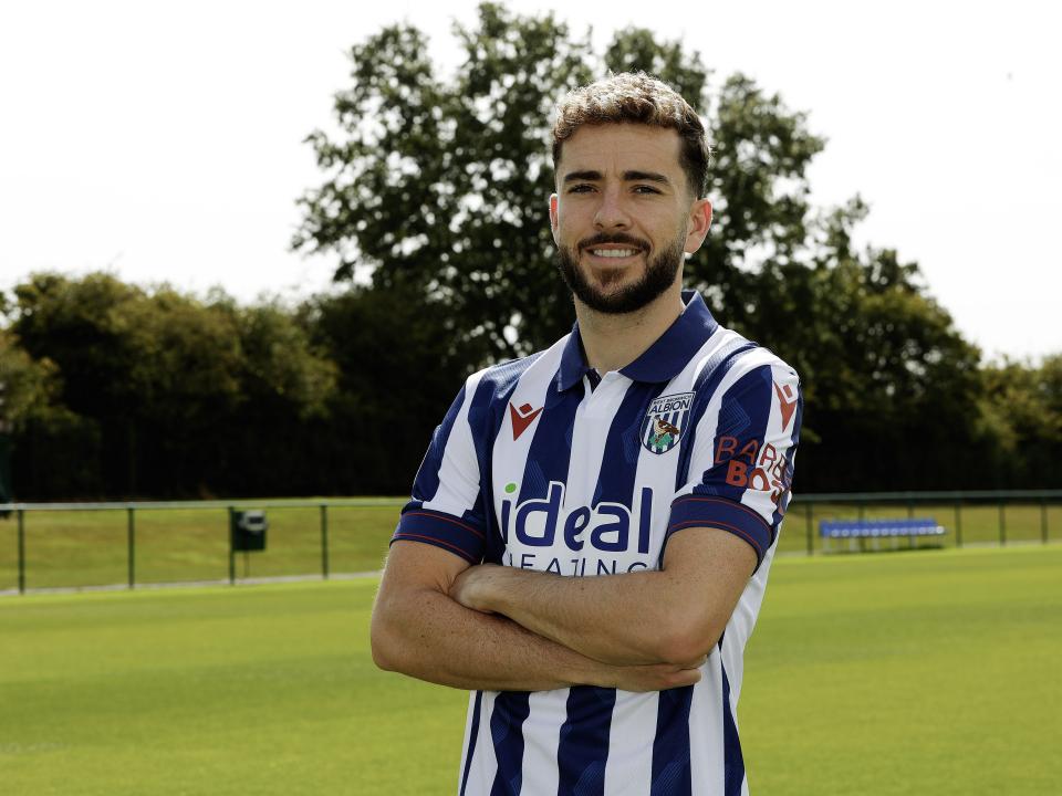 Mikey Johnston smiling at the camera while stood with his arms folded in a home shirt 