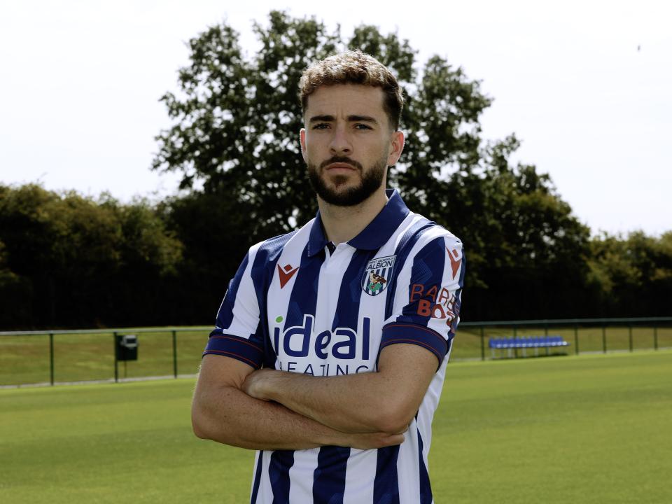Mikey Johnston looking at the camera while stood with his arms folded in a home shirt 