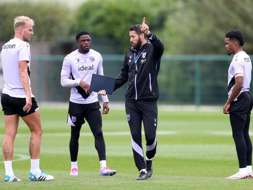 Coach Damia Abella delivering instructions to three players on the training pitch