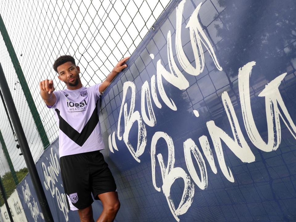 Mason Holgate stood in the home shirt next to a sign which says Boing Boing pointing and smiling at the camera  