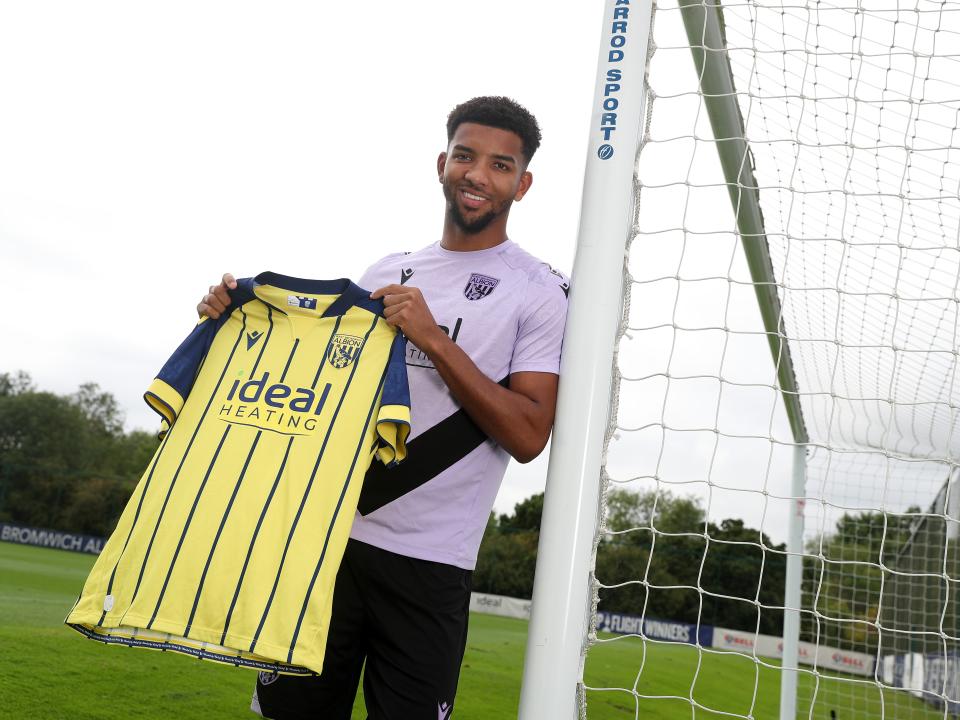 Mason Holgate smiling at the camera holding up a yellow away shirt 